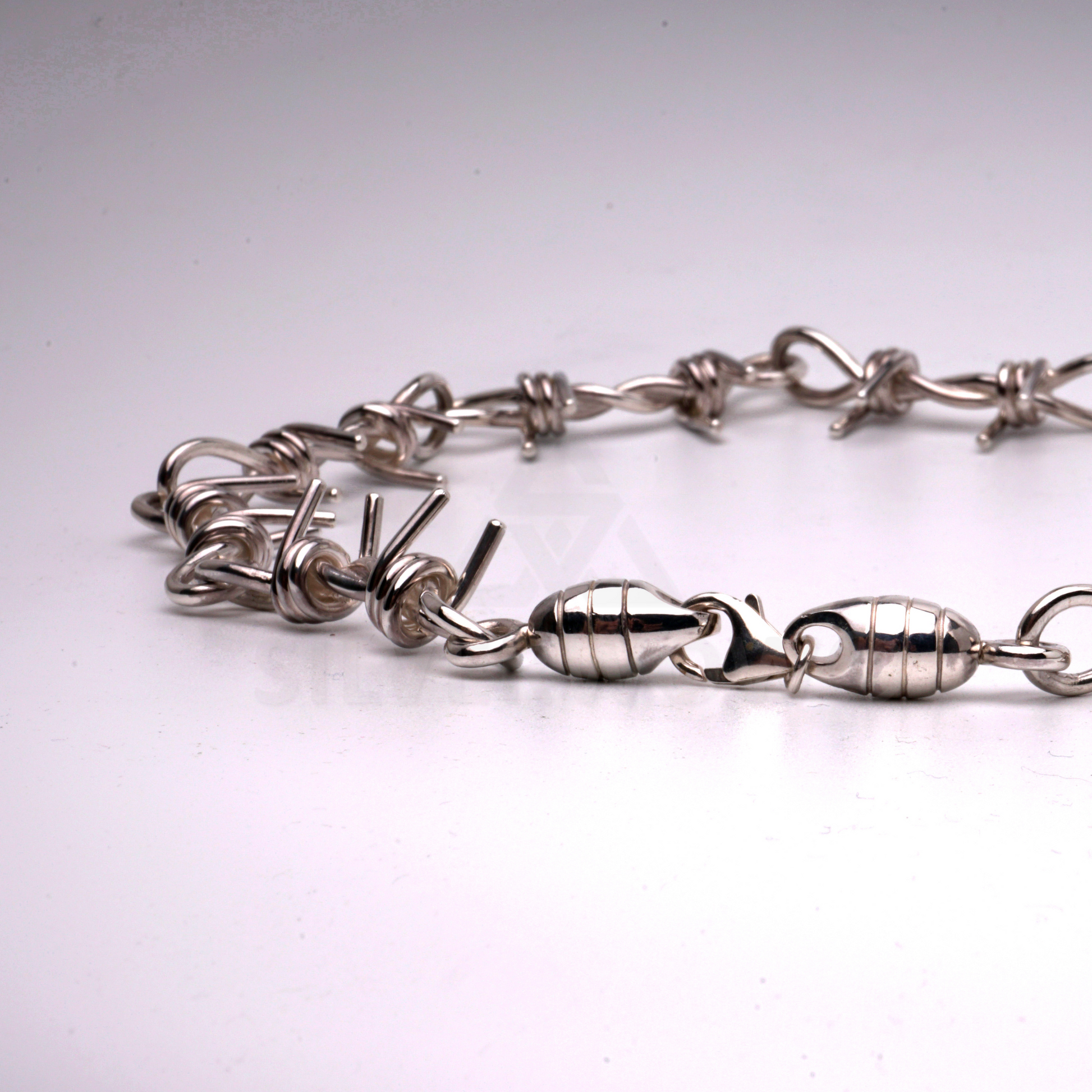 Silver barbed wire necklace laid out straight, showcasing length and construction
