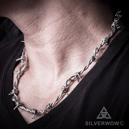 Close-up of silver barbed wire chain necklace worn close around neck
