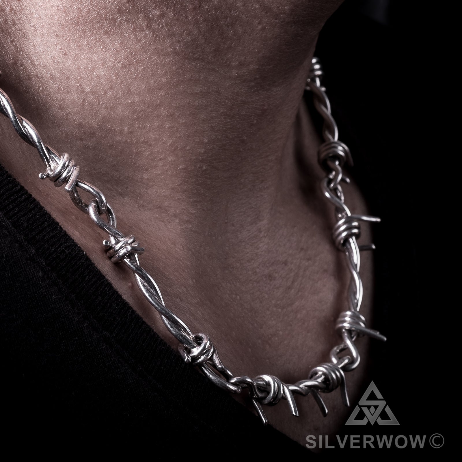 Side view of barbed wire chain necklace in silver, worn in low lighting
