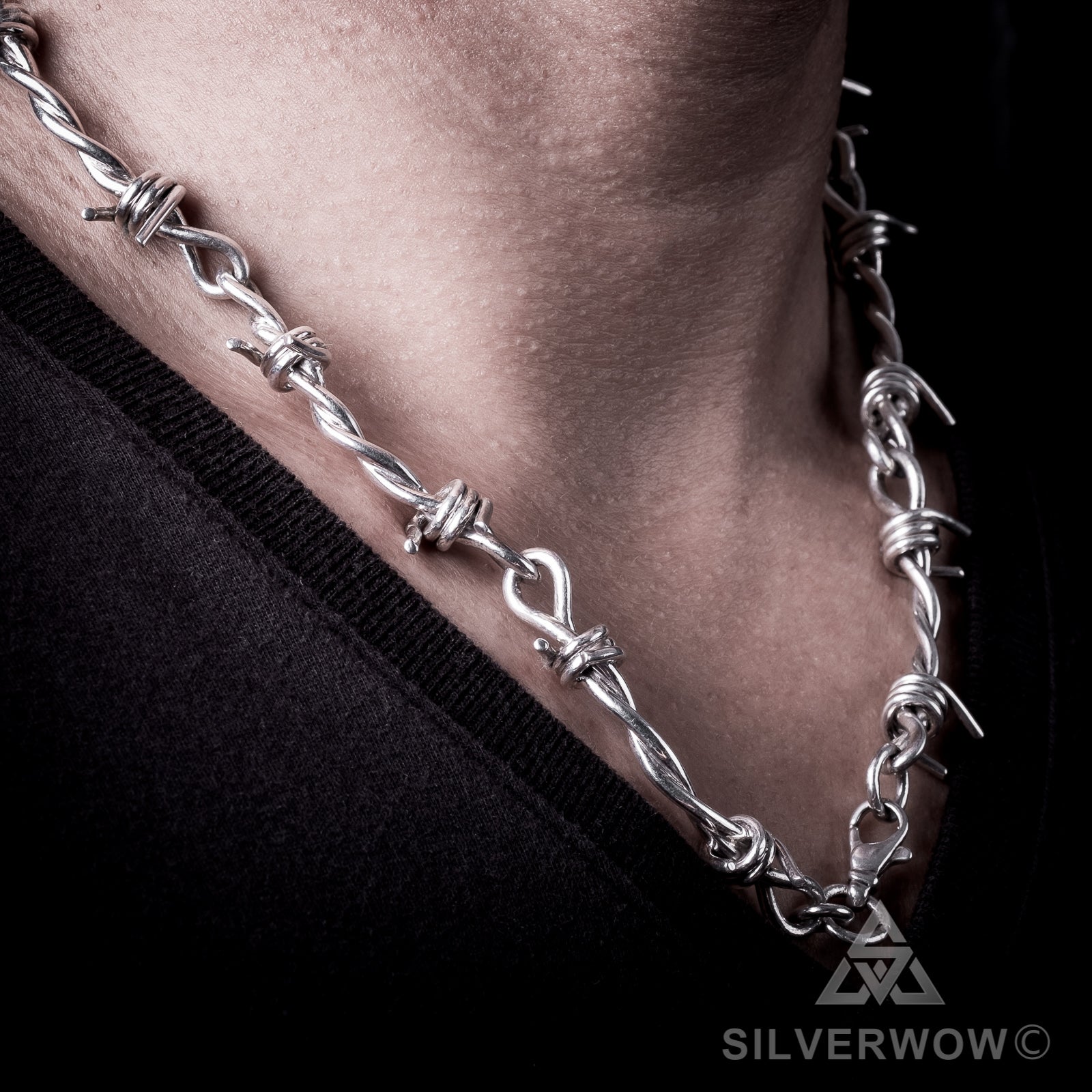 Silver barbed wire necklace around neckline, edge of hair and chain detail visible
