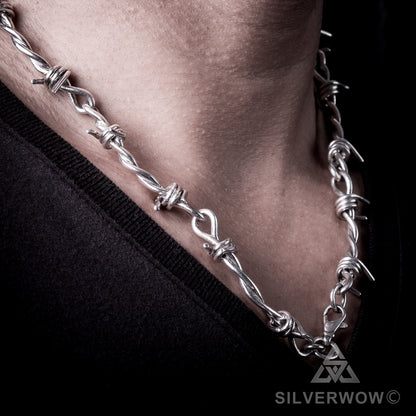 Silver barbed wire necklace around neckline, edge of hair and chain detail visible
